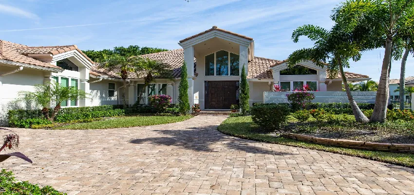 South Florida luxury home exterior with paver driveway, arched entry, and tropical landscaping
