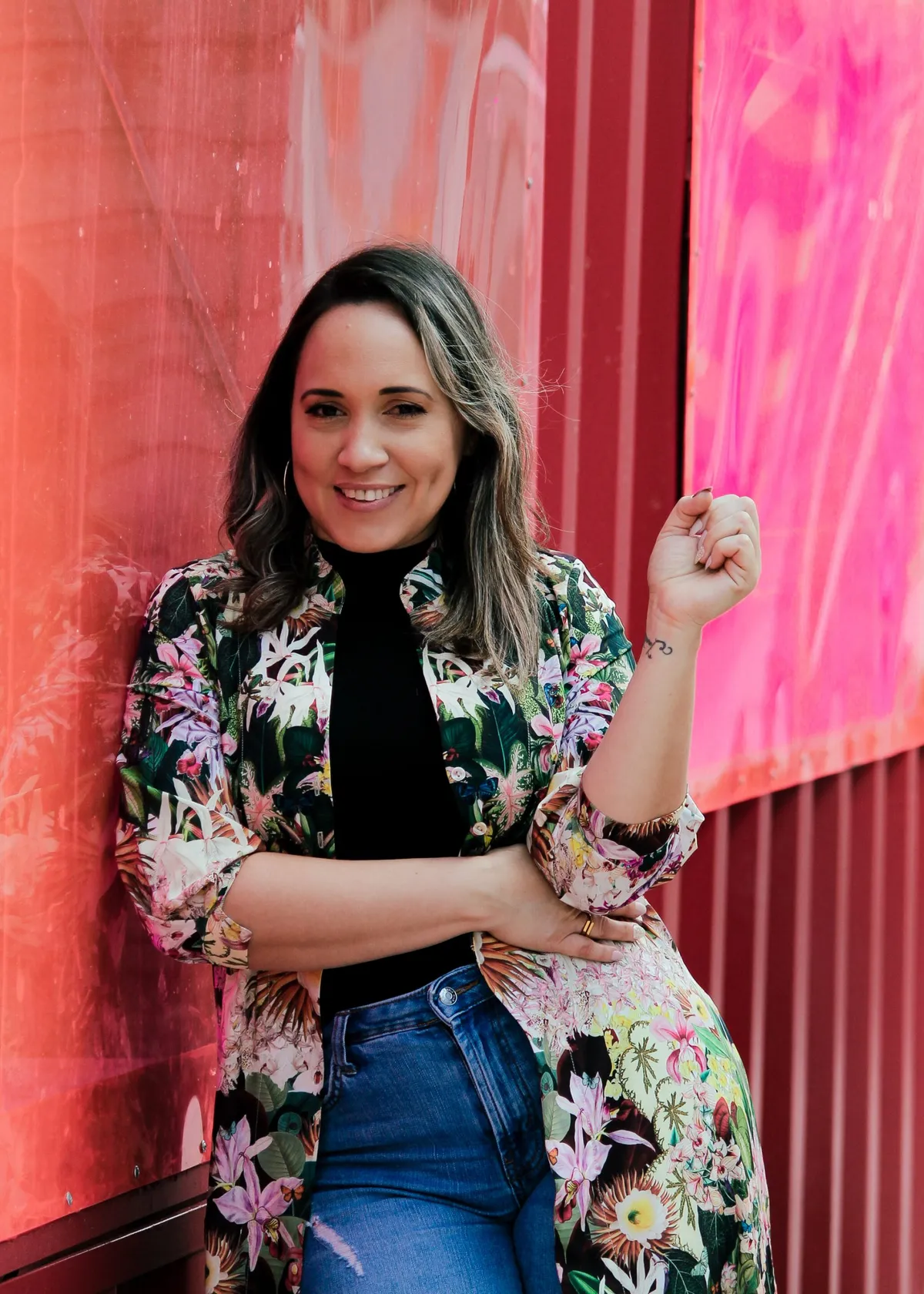 Smiling woman in a floral kimono leaning against a bright red wall, wellness blog portrait