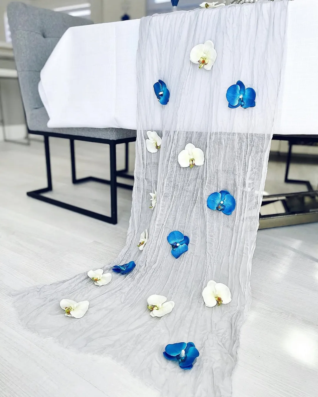 Sheer gray table runner scattered with blue and white silk orchid blooms