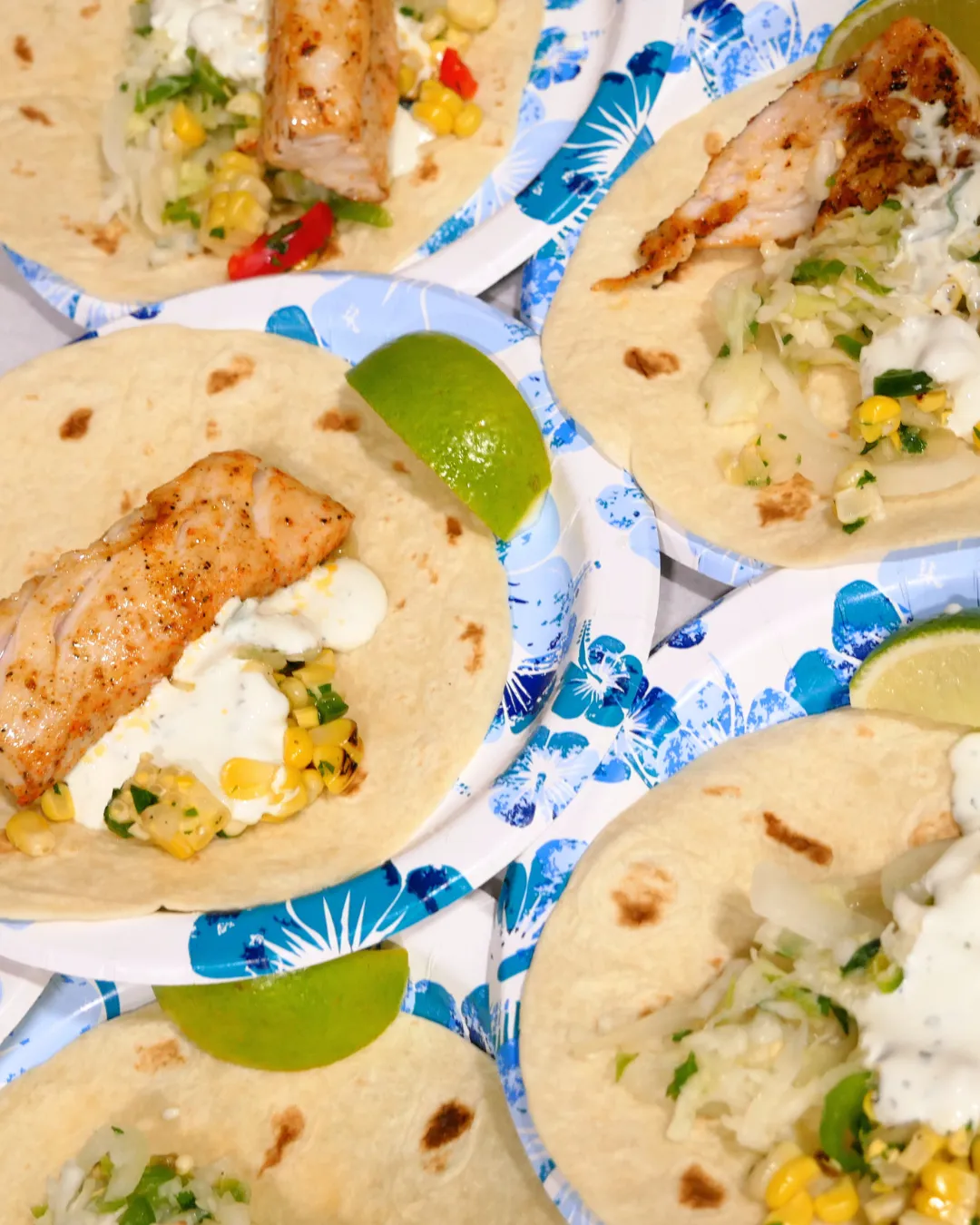 Blackened mahi tacos with corn salsa, sour cream and lime wedges on tropical paper plates