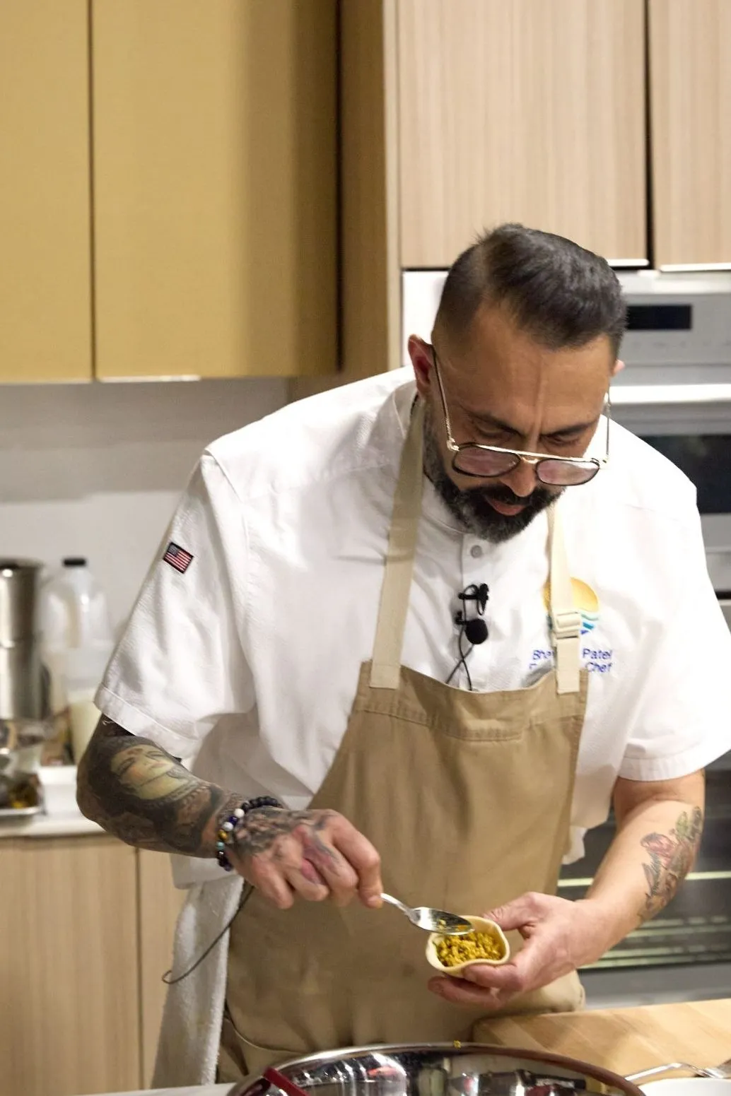 Chef Bhavesh Patel spoons filling into a samosa wrapper while wearing a tan apron