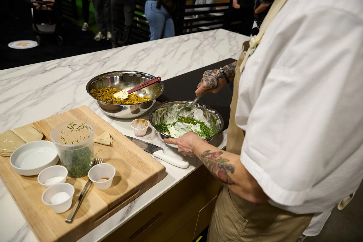 Chef stirs mint yogurt sauce in a metal bowl beside a bowl of spiced filling