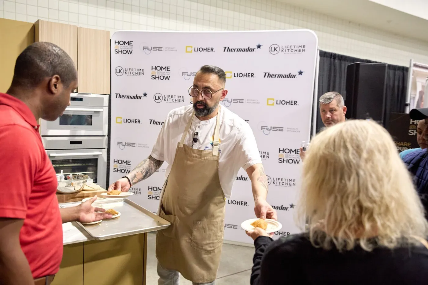 Chef hands out plated samosa samples to attendees in front of sponsor backdrop