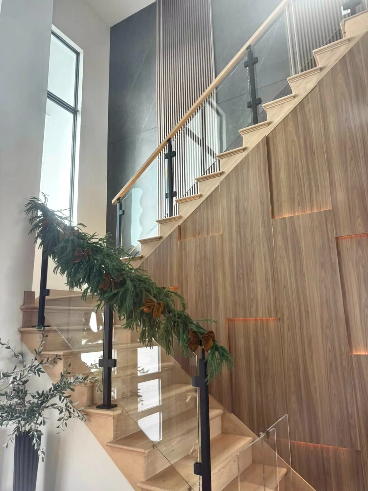 Wooden staircase with glass railing decorated with a pine garland and gold bows