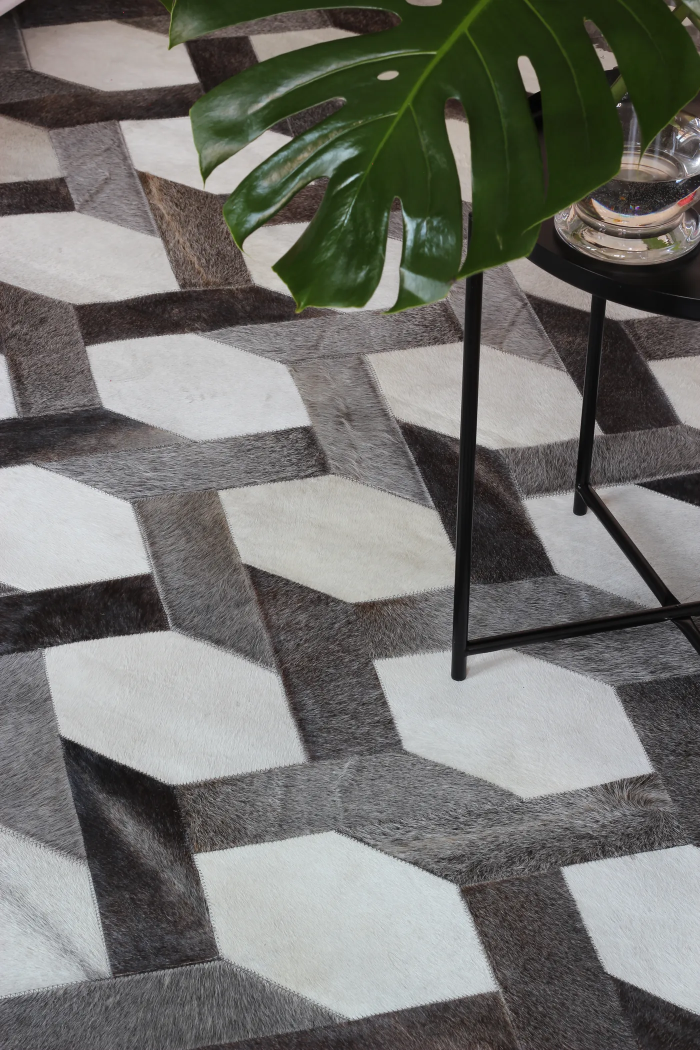 Hexagonal patchwork cowhide rug beneath a black side table with a monstera leaf
