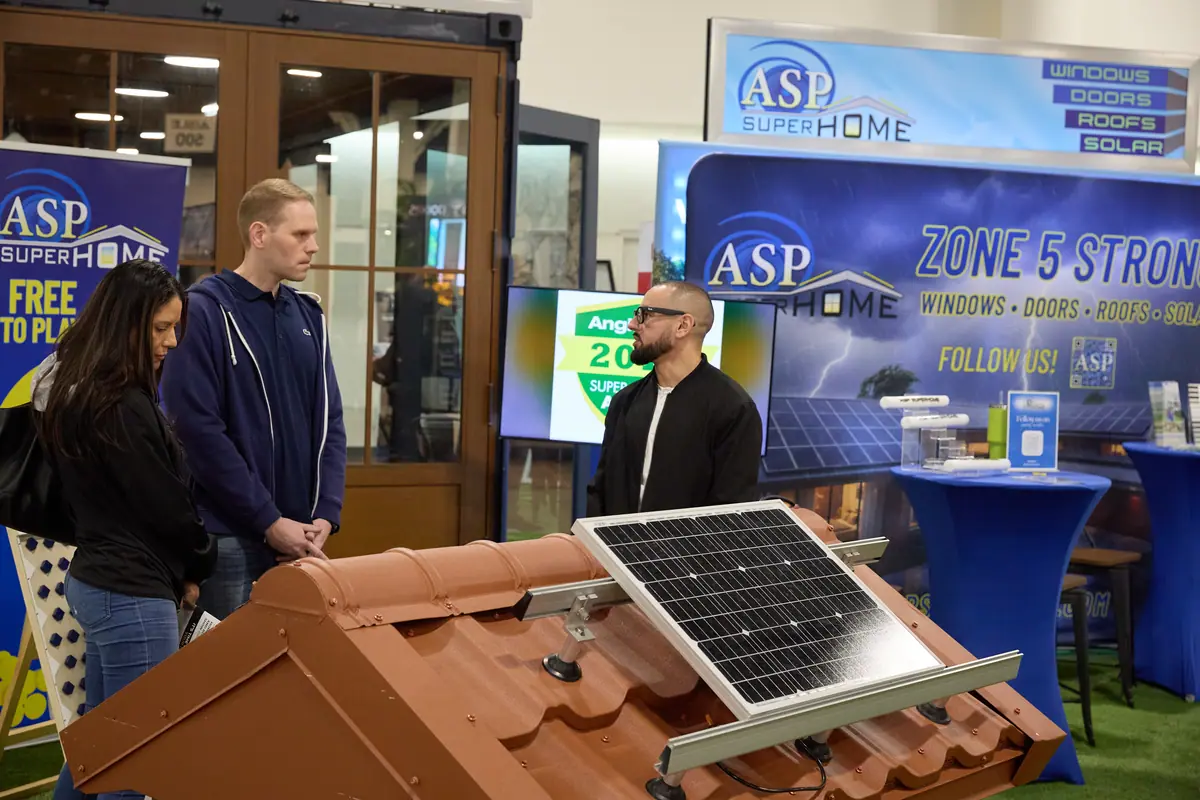 ASP SuperHome booth with attendees examining a solar panel and tile roof model at a home show