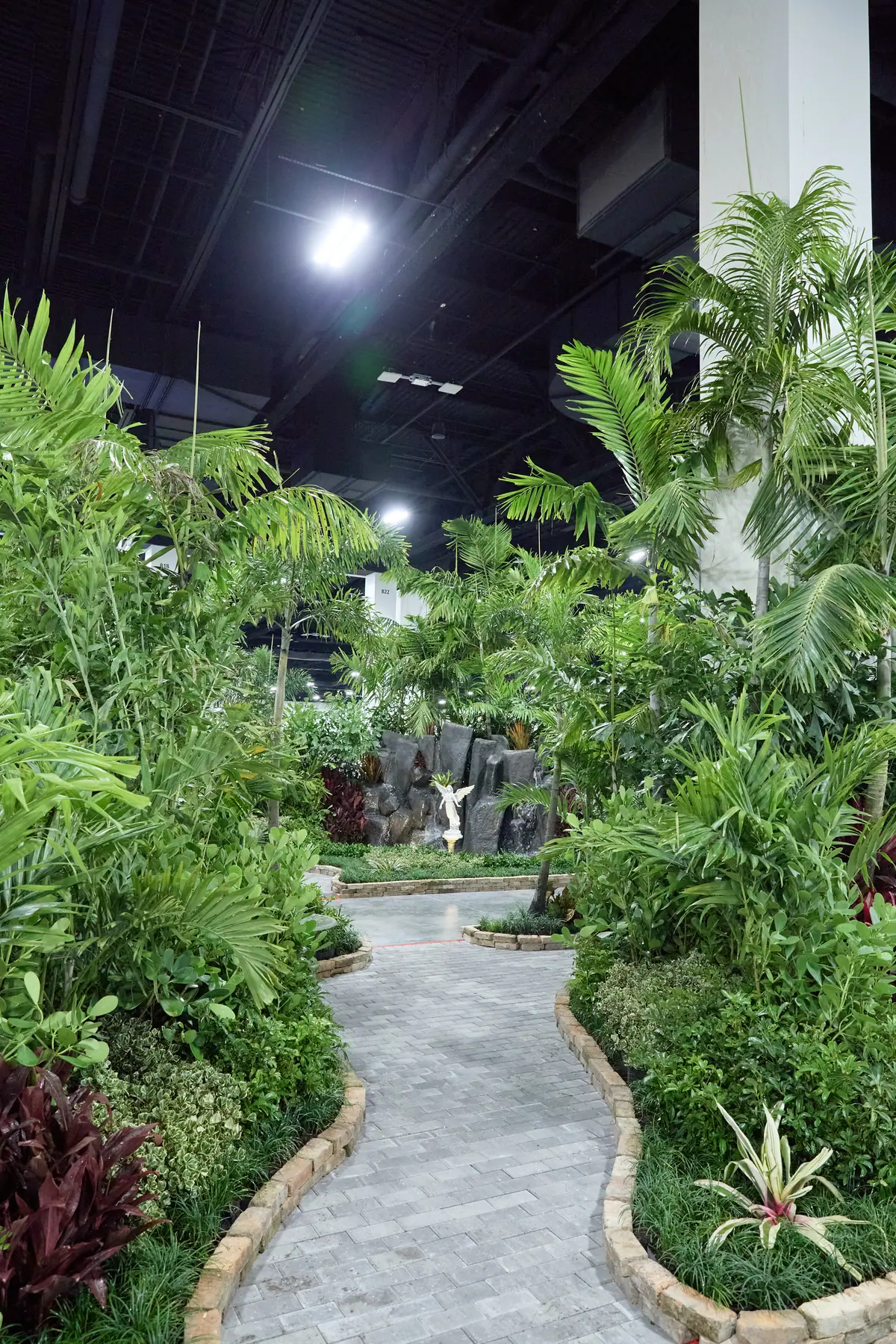 Indoor tropical garden walkway with palm trees and rock waterfall at the home show
