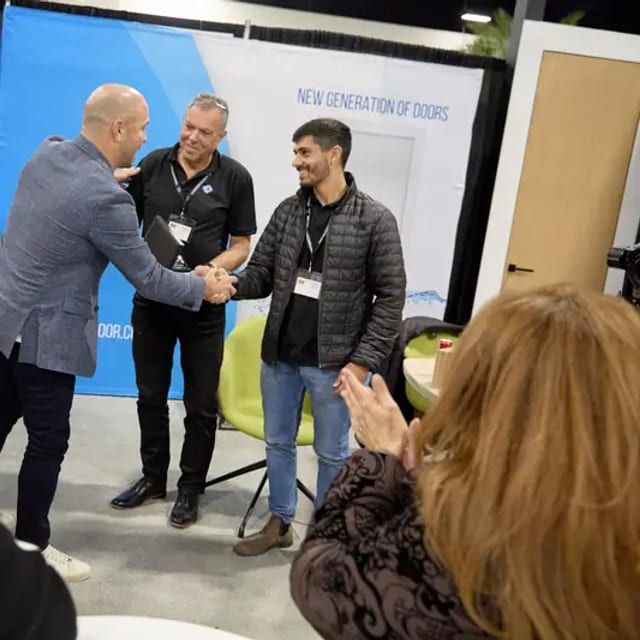 Prize winner shakes hands with an exhibitor at a door company booth as audience applauds